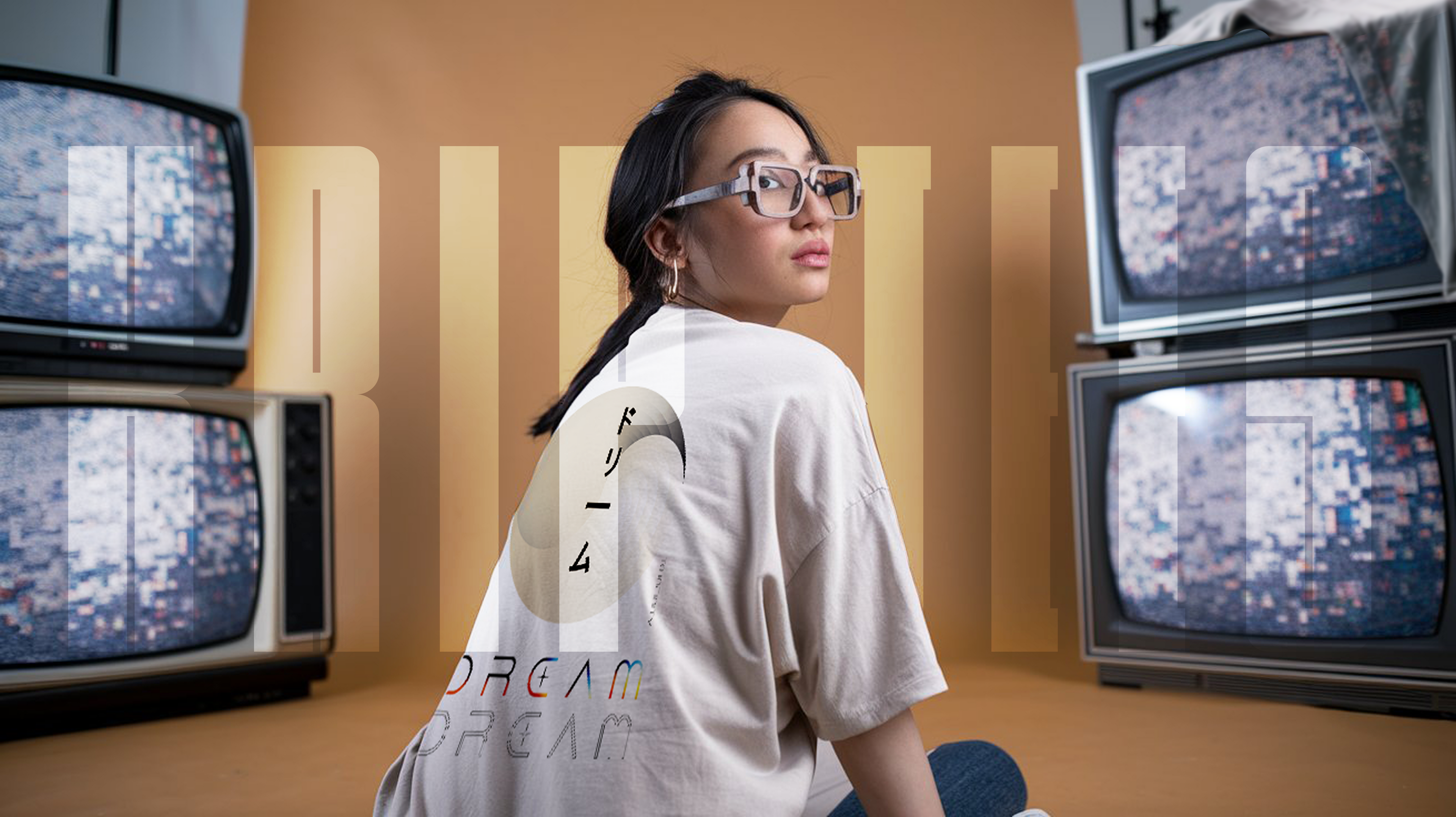 Person wearing glasses sitting among vintage TVs with a blurred background